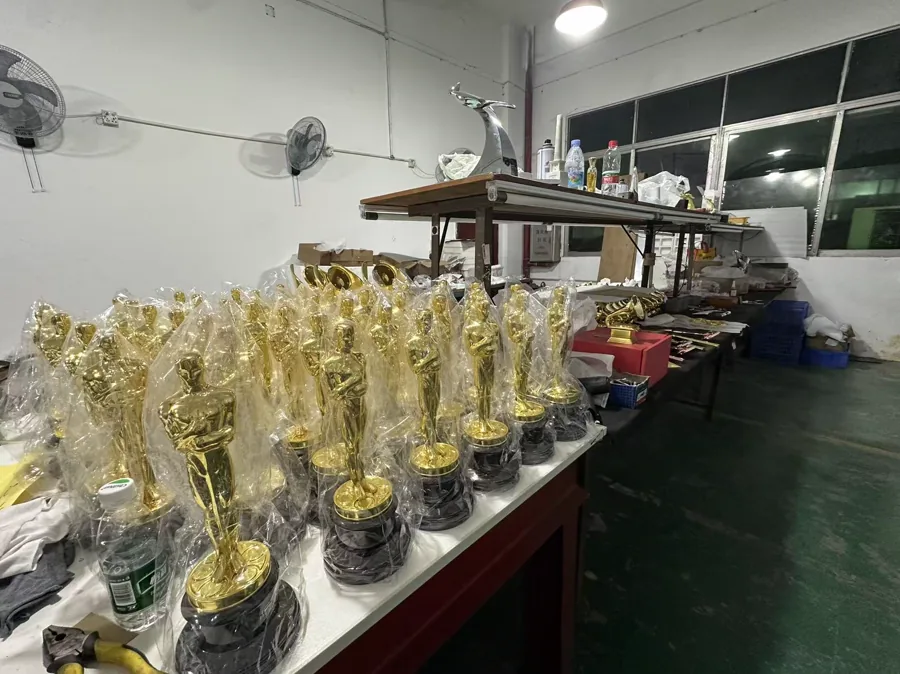 Batches of gold-colored award statuettes awaiting inspection and packing on the production floor